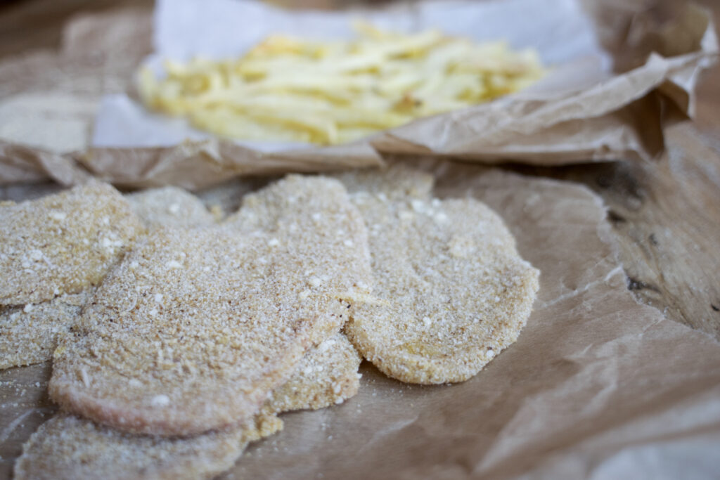 coated chicken cutlets with bread crumbs and some raw potato fries placed on paper