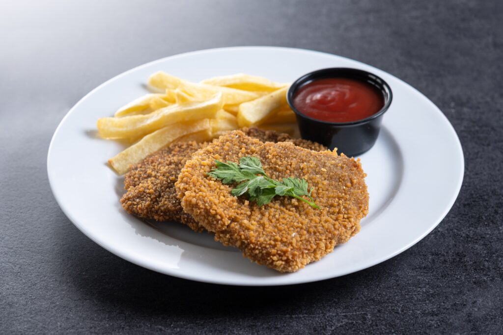 crispy fried chicken cutlets served in a white ceramic plate with fries and ketchup 