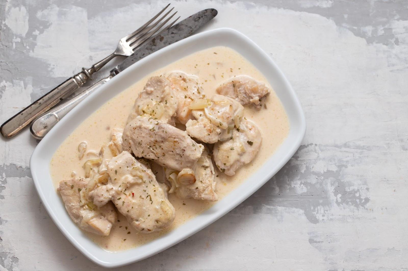 Chicken cutlets marinating in buttermilk with spices inside a white dish.