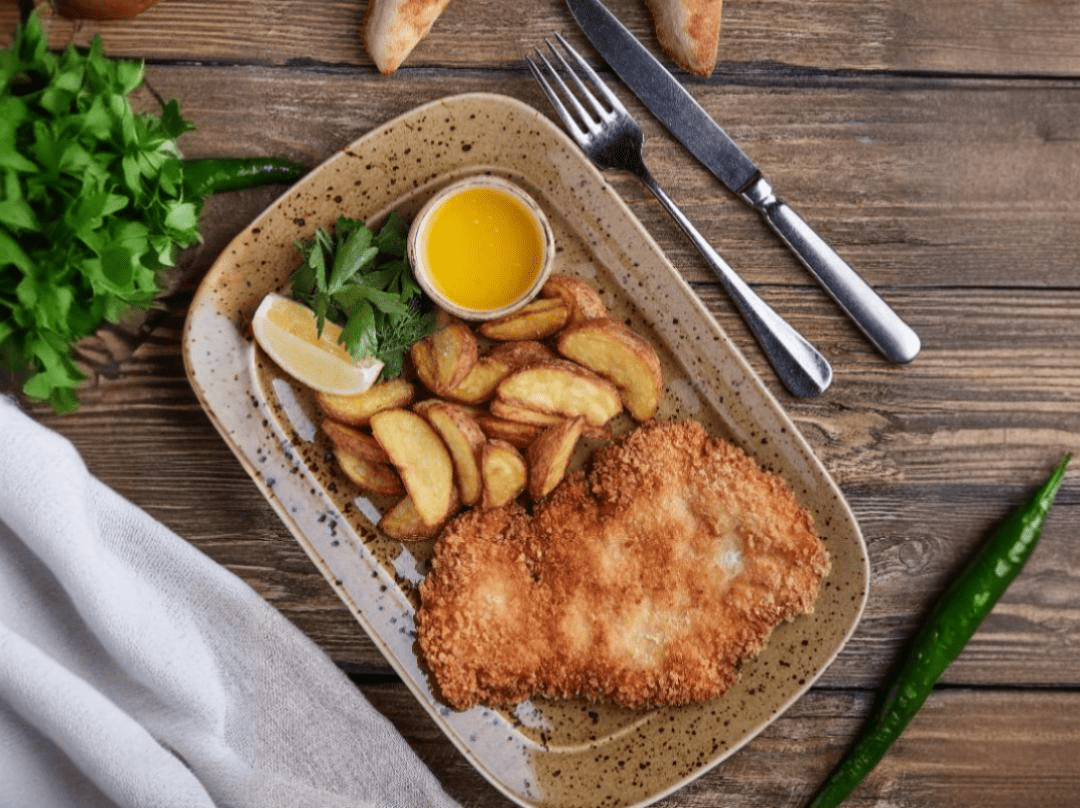 Chicken Schnitzel served with potato wedges, sauce and lemon