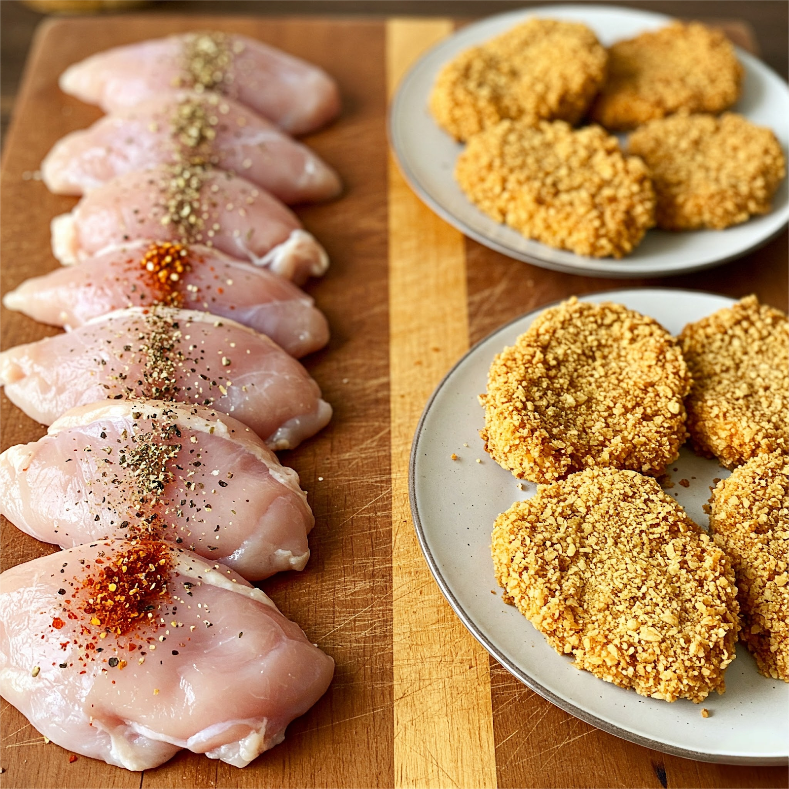 on a wooden board on left side raw chicken cutlets are being seasoned with salt, pepper, garlic powder, and smoked paprika. on right side breaded cutlets are placed in plates