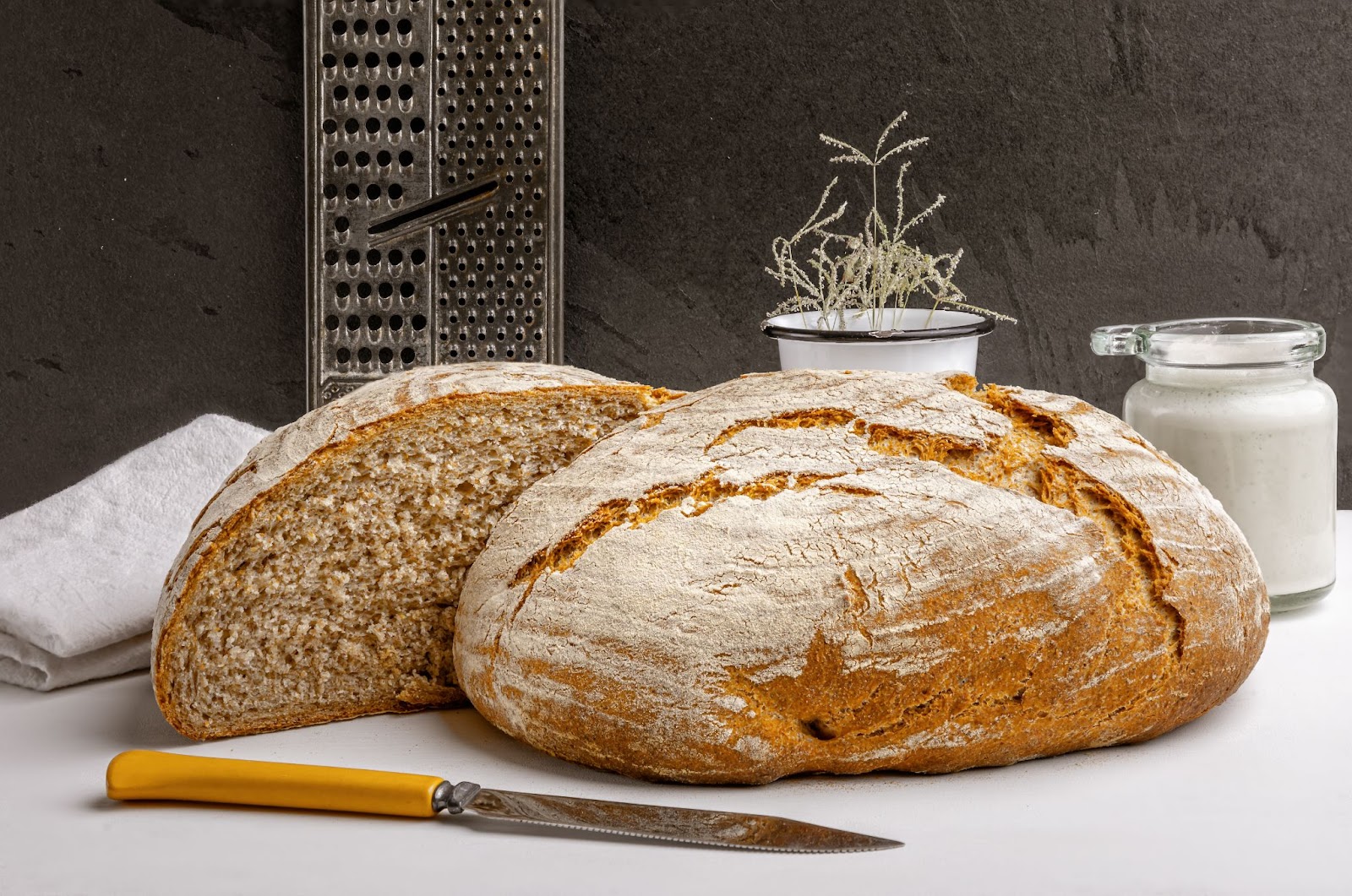 one whole and one half cut Sourdough displayed on white table top with knife in front 