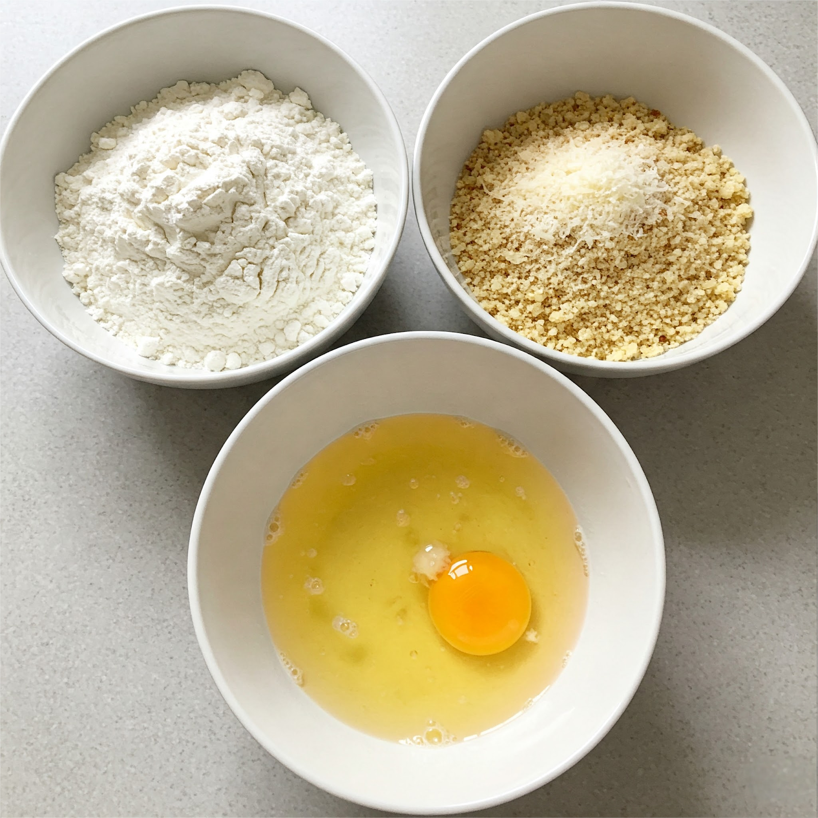3 bowls placed on table top filled with flour in one bowl, beaten egg in another, mix breadcrumbs and Parmesan in a third bowl.