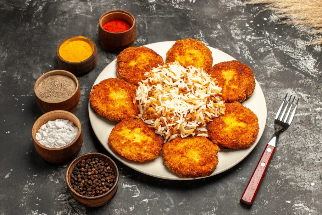 cutlets being served in a plate with some rice along with some spices bowls beside the plate