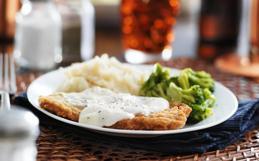 crispy cutlet with gravy served in white plate with lettuce