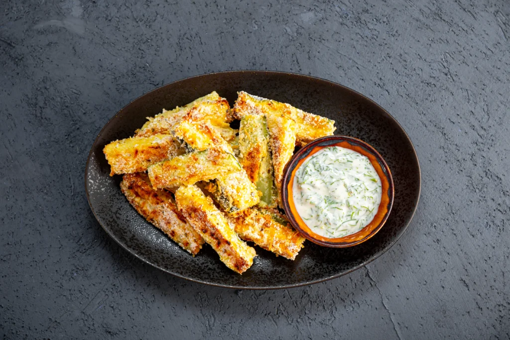 zucchini fries with white sauce in side served in black plate
