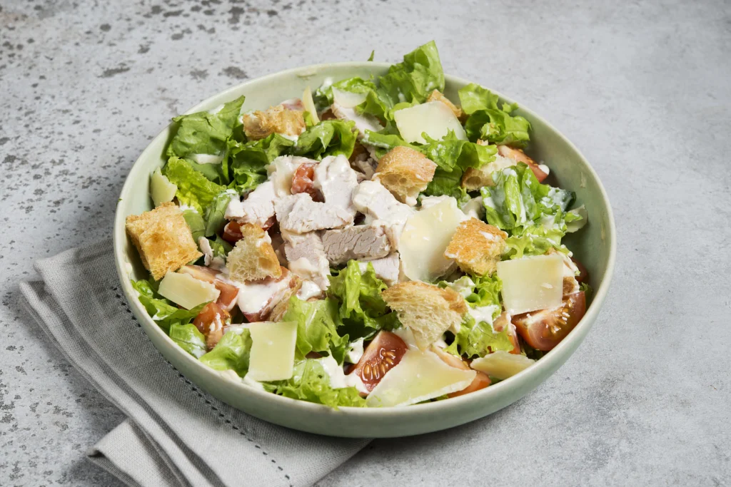 homemade caesar salad with croutons and parmesan served in a white bowl placed on table top